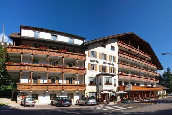 Hotel s dřevěnými balkony a vozy zaparkovanými vpředu.