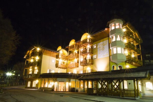 Nočně osvětlený vícepatrový hotel s dřevěnými balkony.