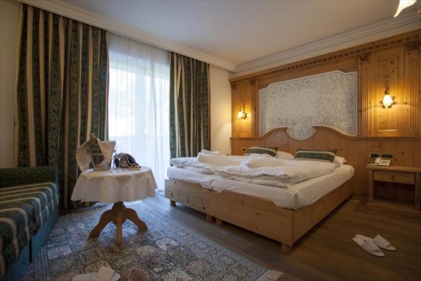 Elegantní hotelový pokoj s manželskou postelí a dřevěným obložením.