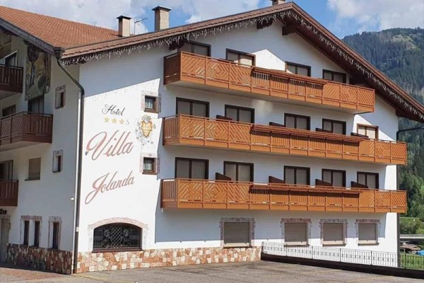 Bílá budova hotelu Villa Jolanda s dřevěnými balkony a nápisem na fasádě.