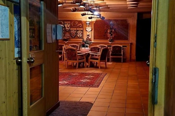 Pohled do dřevěného interiéru s jídelním stolem a židlemi, osvětlený teplými světly.