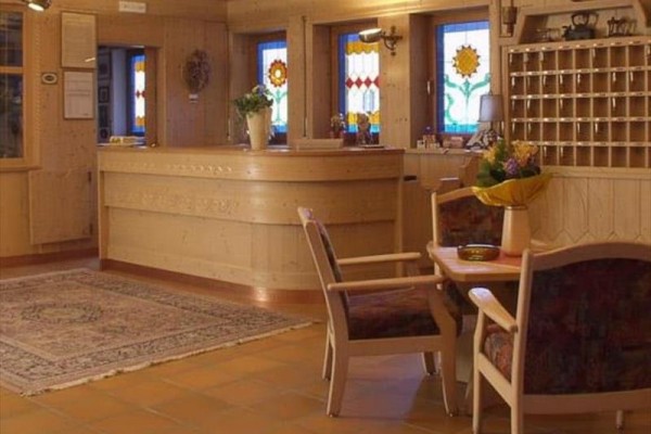 Hotelová recepce s dřevěným nábytkem a barevnými vitrážovými okny.