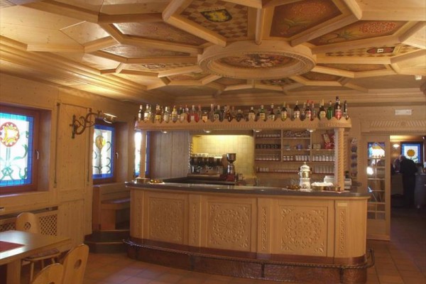Dřevěný interiér kavárny s barem, lahvemi alkoholu a vitrážovými okny.  