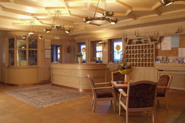 Recepce s dřevěným nábytkem a dekoracemi, vitrážovými okny a koberci.
