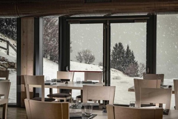 Restaurace s dřevěnými židlemi a stoly s výhledem na zasněženou krajinu.