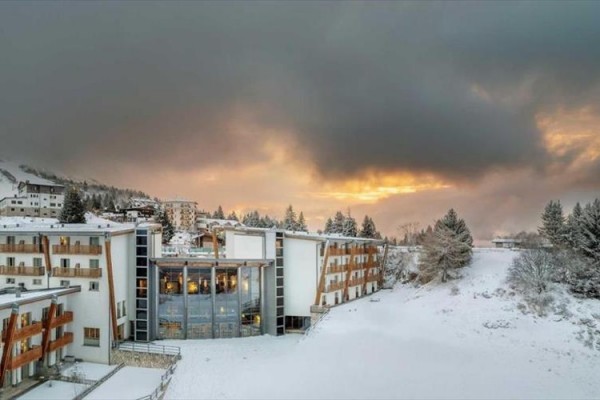 Zimní horská krajina s budovou hotelu pod zataženou oblohou při západu slunce.