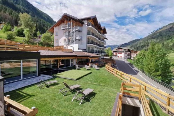 Moderní budova hotelu obklopená horami a zelení, s lehátky na trávníku.