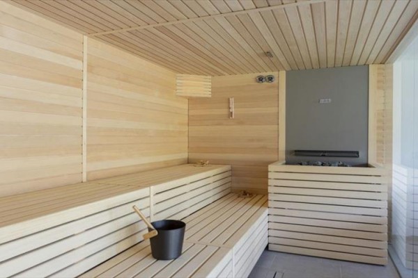 Interiér moderní sauny s dřevěnými lavicemi a kovovým vědrem.