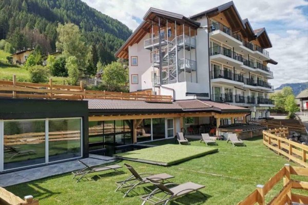 Horský hotel s terasou a lehátky na zeleném travnatém prostranství.