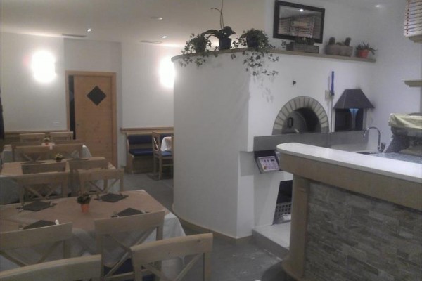 Interiér restaurace s dřevěnými stoly a kamennou pecí.