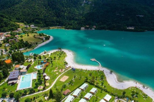 Letecký pohled na tyrkysové jezero obklopené zelenou krajinou a zástavbou.