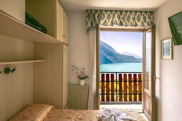 Pokoj s výhledem na jezero a hory za otevřenými dveřmi na balkon.
