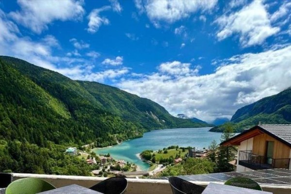 Jezero obklopené zelenými horami pod modrou oblohou s mraky, viděné z terasy.