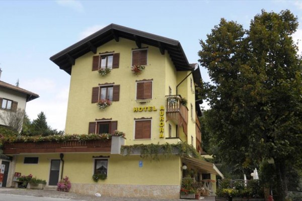Žlutá budova hotelu s květinami na balkonech obklopená stromy.