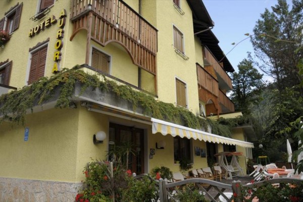 Žlutá budova hotelu Aurora s dřevěnými balkony a venkovní zahrádkou.