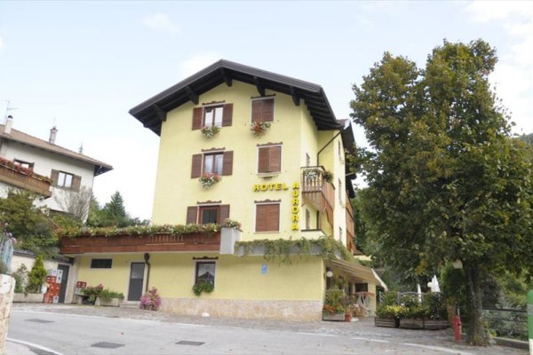Třípatrový žlutý hotel s dřevěnými okenicemi a květinami na balkonech u silnice.