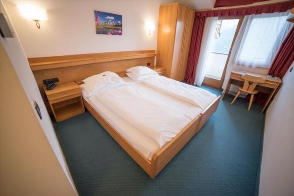 Hotelový pokoj s manželskou postelí, psacím stolem a balkonem.