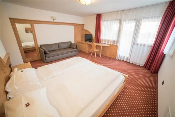 Pokoj v hotelu s dvojlůžkem, pohovkou, psacím stolem a televizí.