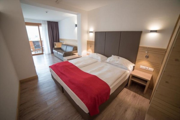 Moderní hotelový pokoj s manželskou postelí, červenou přikrývkou a balkónem.