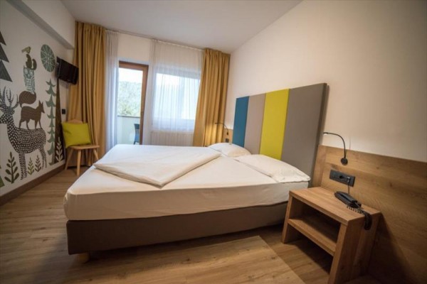 Moderní hotelový pokoj s dvojlůžkem, barevnou čelní stěnou a nástěnnou malbou zvířat.