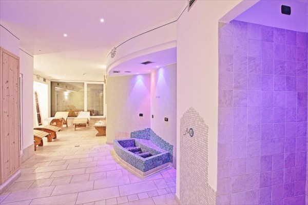 Moderní wellness centrum s lehátky a vodními objekty pod fialovým osvětlením.