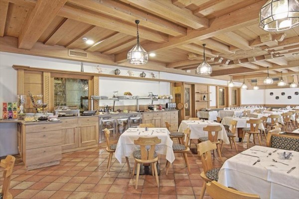 Prostorná restaurace s dřevěným interiérem a jídelními stoly pokrytými bílými ubrusy.