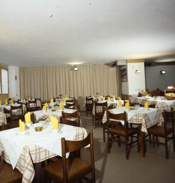 Restaurace s dřevěnými židlemi a stoly pokrytými bílými ubrusy a žlutými ubrousky.