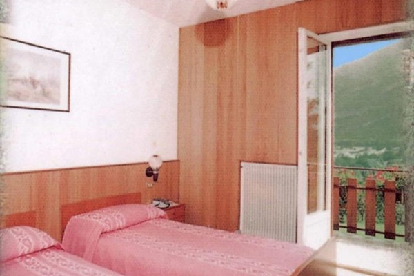 Pokoj se dvěma postelemi s růžovým povlečením a otevřenými dveřmi na balkon.