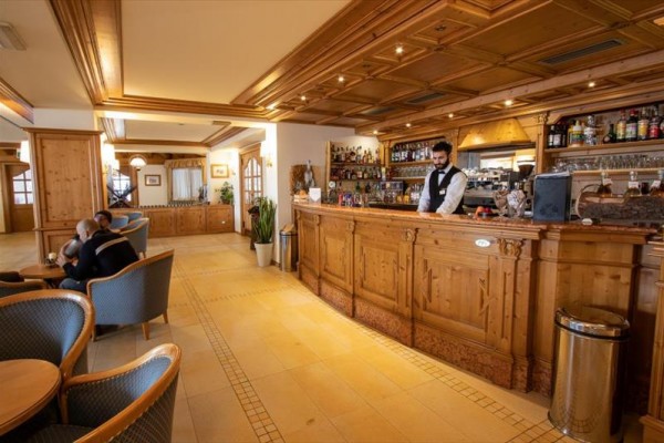 Dřevěný bar s barmanem v elegantním interiéru s hosty sedícími v křeslech.