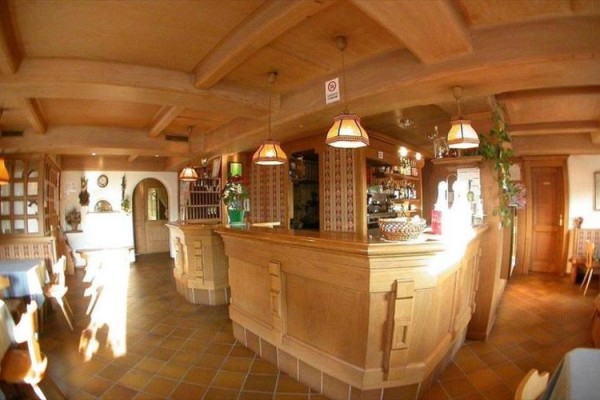 Interiér útulné restaurace s dřevěným nábytkem a barem.  