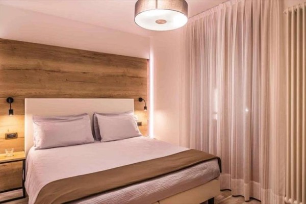 Moderně zařízená ložnice s dřevěnou stěnou, manželskou postelí a elegantním osvětlením.