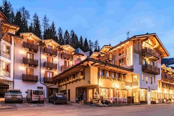 Malebný horský hotel v podvečer se světlými okny a dřevěnými balkony.