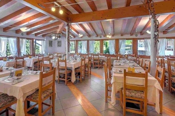 Restaurace s dřevěnými stoly a židlemi, prostřenými stoly a velkými okny.