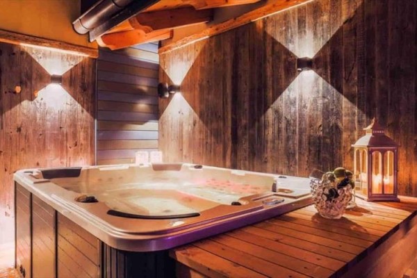 Vnitřní jacuzzi obklopené dřevěnými panely s osvětlením a lucernou na stole.