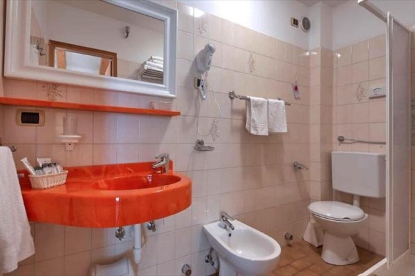Koupelna s oranžovým umyvadlem, toaletou a bidetem.