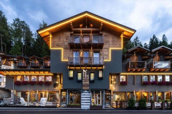 Moderní horský hotel s dřevěným obložením a osvětlením, obklopen lesem.