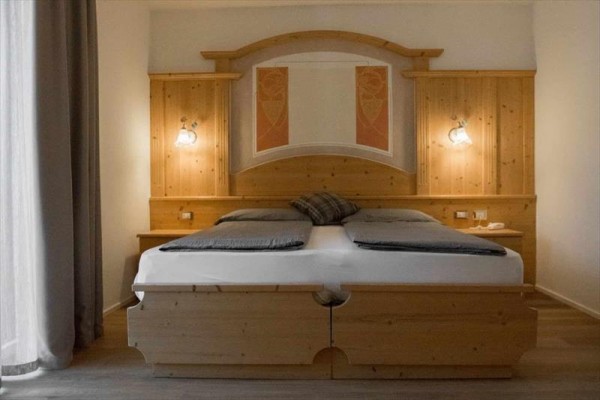 Dřevěná manželská postel s nočními stolky a lampami po obou stranách.