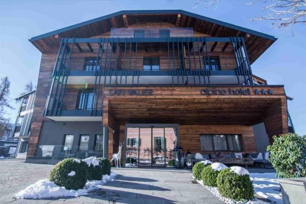 Moderní alpský hotel s dřevěným obložením a proskleným vstupem.