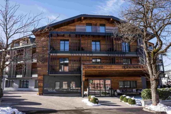 Moderní dřevěný hotel s balkony a stromy v popředí.
