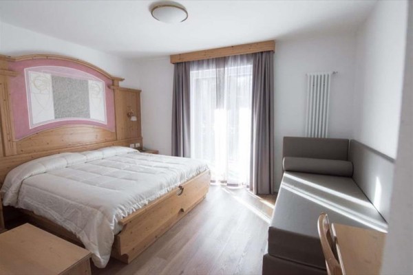 Ložnice s dřevěným dvojlůžkem, pohovkou a závěsy na okně.