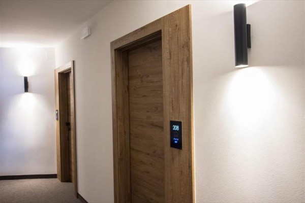 Chodba s dřevěnými dveřmi a světly na stěnách.