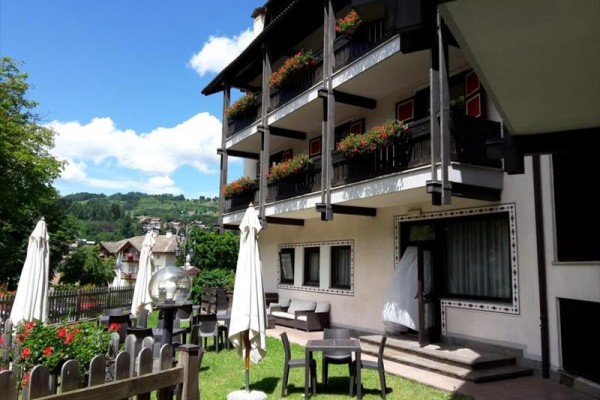 Třípatrová budova s květinovými truhlíky na balkonech, obklopená zahradou s venkovním posezením.