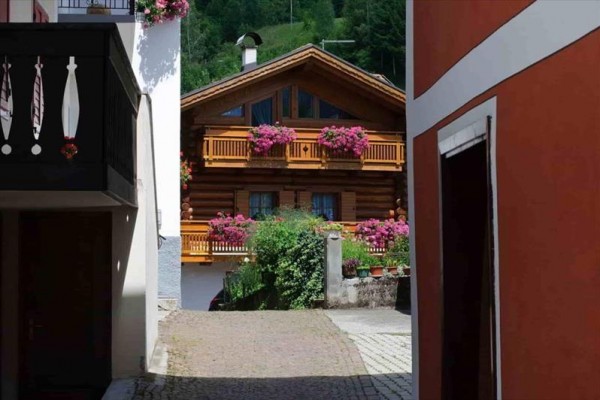Dřevěný chalupový dům s květinami na balkonech mezi dvěma budovami.