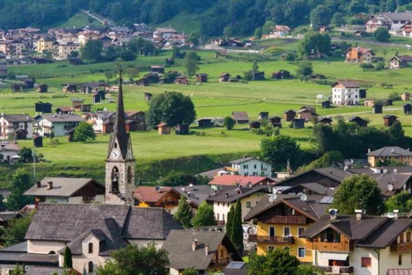 Malebná vesnice se špičatou věží kostela obklopená zelenými kopci.