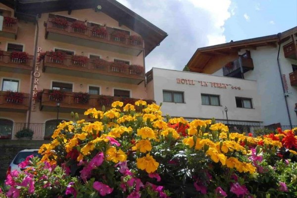 Hotel s květinami na předzahrádce pod balkony s dřevěnými zábradlím.