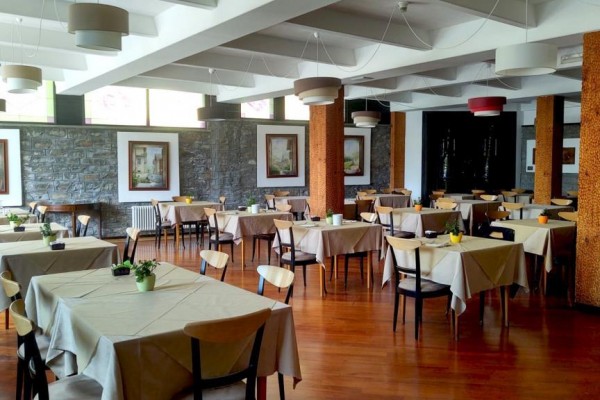 Restaurace s dřevěnou podlahou, kulatými stoly a obrazy na stěnách.  