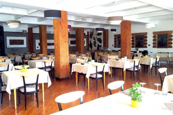 Restaurace s dřevěnými sloupy a stoly pokrytými bílými ubrusy.