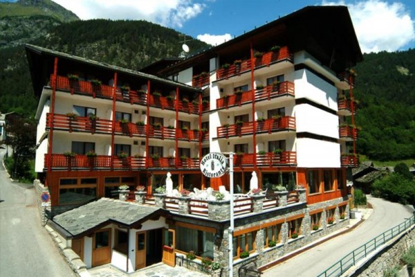 Velký hotel s dřevěnými balkony mezi horami a lesem.