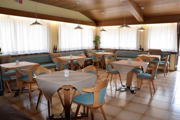 Restaurace se světle dřevěným nábytkem a bílými závěsy.
