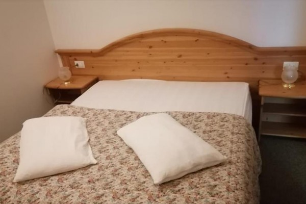 Manželská postel s dřevěným čelem a květinovým přehozem.